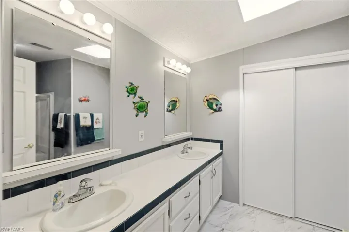Full bathroom with double vanity, a textured ceiling, light marble finish flooring, a stall shower, and ornamental molding