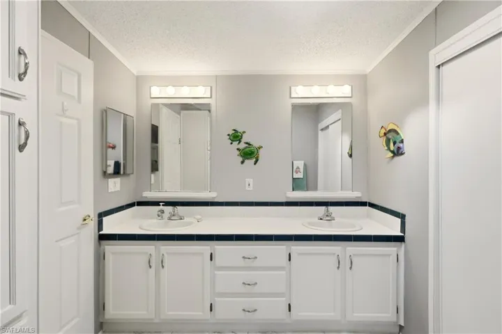 Bathroom with double vanity, a textured ceiling, and ornamental molding