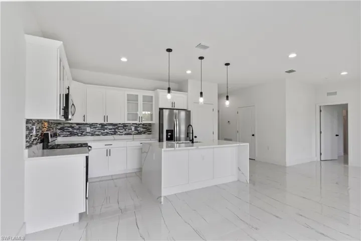 Kitchen with appliances with stainless steel finishes, recessed lighting, decorative backsplash, white cabinetry, and a kitchen island with sink