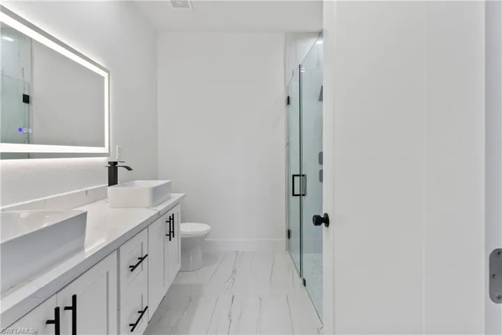 Bathroom with double vanity, marble look tiles, and a shower stall