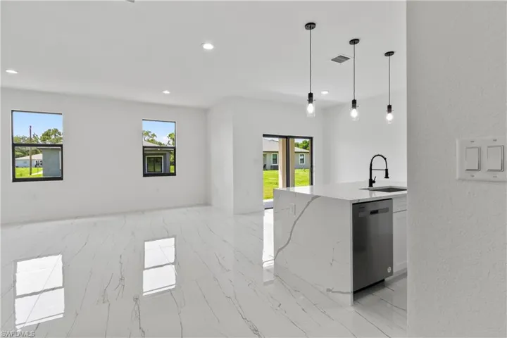 Kitchen with open floor plan, light marble finish floors, light stone counters, dishwasher, and healthy amount of natural light