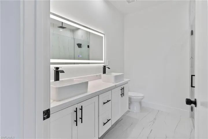 Bathroom with a marble finish shower, double vanity, and marble look tile flooring