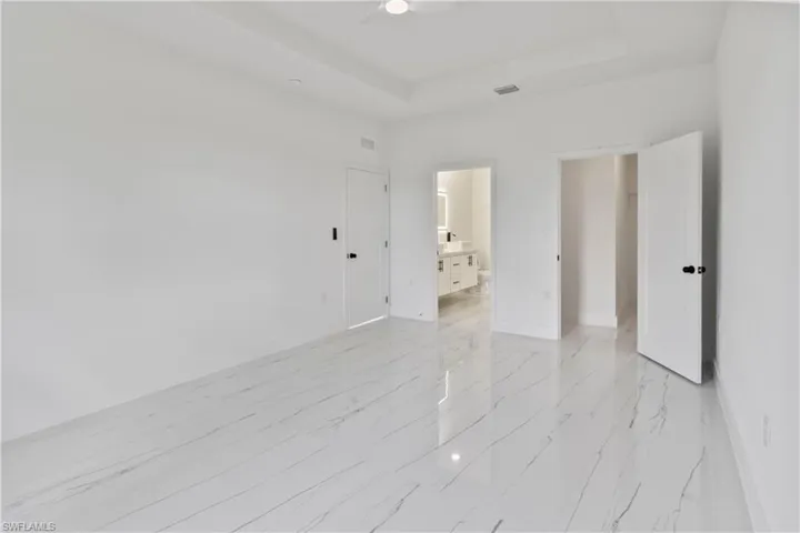 Unfurnished room featuring a ceiling fan, a raised ceiling, and light marble finish floors