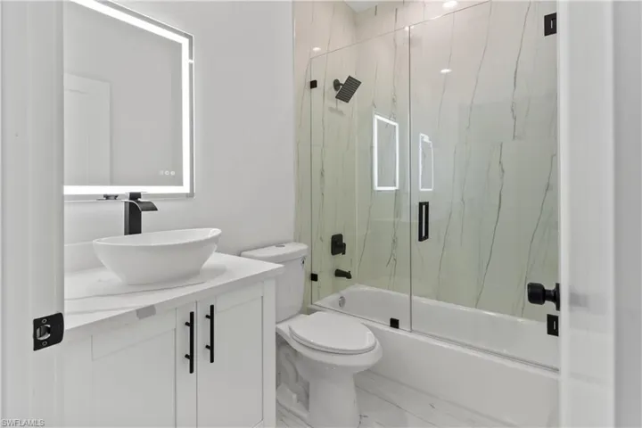Bathroom with combined bath / shower with glass door, vanity, and marble finish flooring