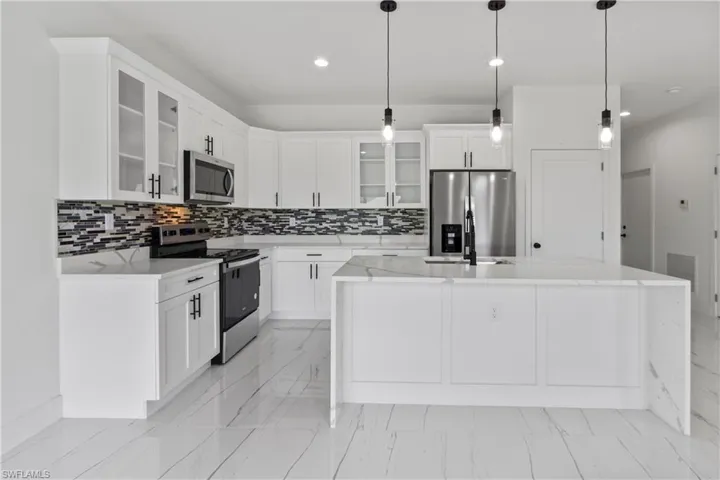 Kitchen with stainless steel appliances, light marble finish flooring, a center island with sink, tasteful backsplash, and recessed lighting
