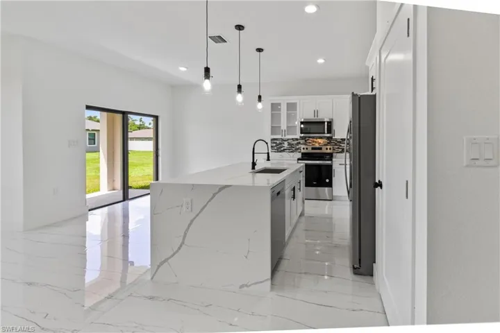 Kitchen featuring light marble finish floors, appliances with stainless steel finishes, tasteful backsplash, a kitchen island with sink, and recessed lighting