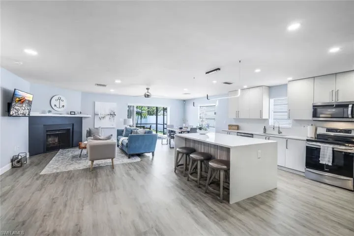 Kitchen with light wood-type flooring, a kitchen island, appliances with stainless steel finishes, white cabinets, and decorative light fixtures