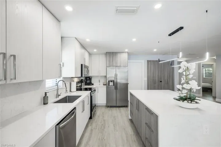 Kitchen featuring hanging light fixtures, light stone countertops, light hardwood / wood-style flooring, stainless steel appliances, and sink