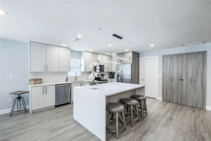 Kitchen with light hardwood / wood-style floors, a center island, appliances with stainless steel finishes, sink, and pendant lighting