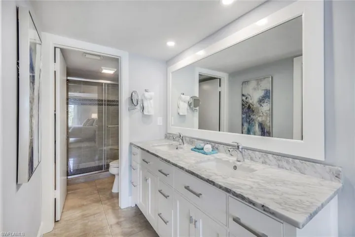 Bathroom featuring tile flooring, double sink, a shower with door, toilet, and large vanity