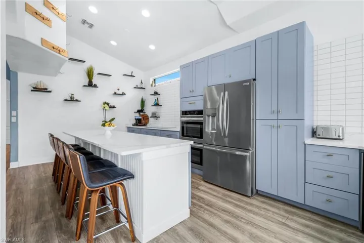 Kitchen featuring a breakfast bar, decorative backsplash, appliances with stainless steel finishes, vaulted ceiling, and light wood finished floors