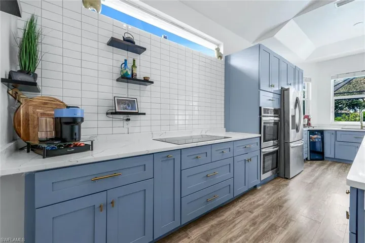 Kitchen with open shelves, blue cabinetry, light stone countertops, and backsplash