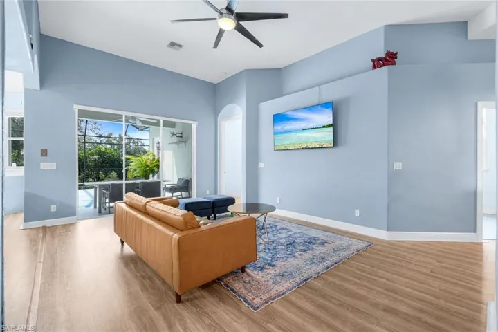 Living room with a ceiling fan, light wood finished floors, arched walkways, and a sunroom