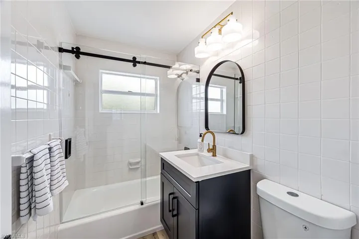 Bathroom with enclosed tub / shower combo, vanity, and tile walls