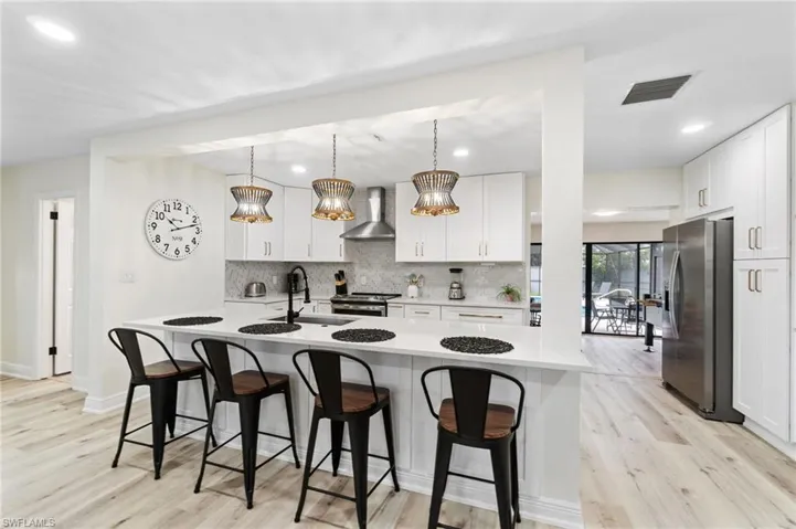 Kitchen with decorative light fixtures, stainless steel appliances, white cabinets, a kitchen bar, and light wood-style floors