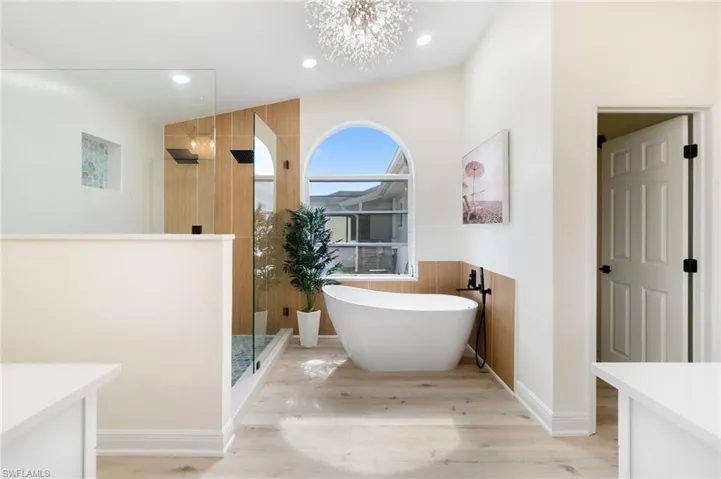 Bathroom with walk in shower, a freestanding bath, light wood-type flooring, a chandelier, and wainscoting