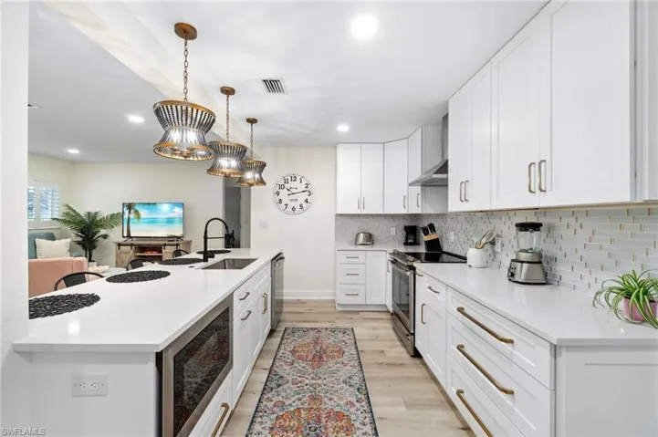 Kitchen featuring stainless steel appliances, decorative light fixtures, white cabinetry, light stone counters, and light wood-style flooring