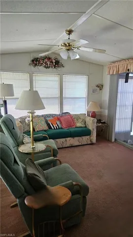Carpeted living room featuring ceiling fan, lofted ceiling, and a textured ceiling