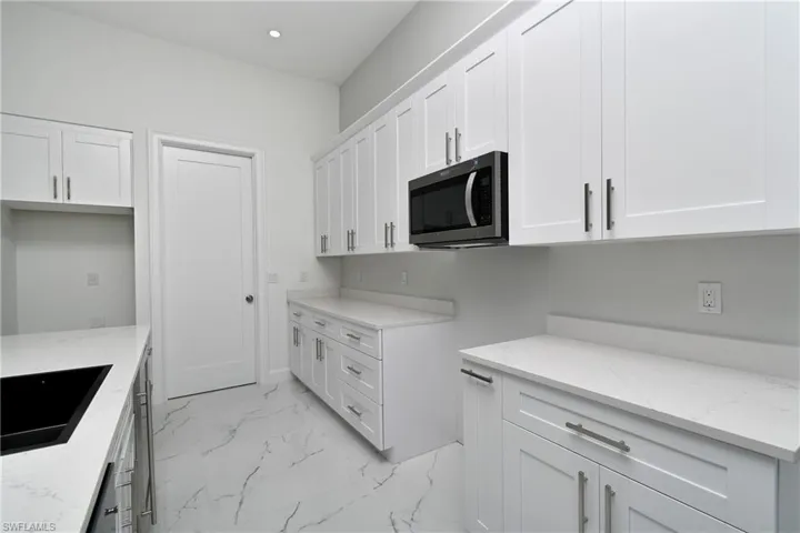 Kitchen with sink, light stone counters, and white cabinetry