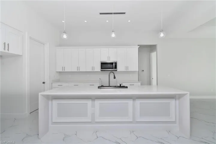 Kitchen featuring pendant lighting, white cabinets, a center island with sink, and sink