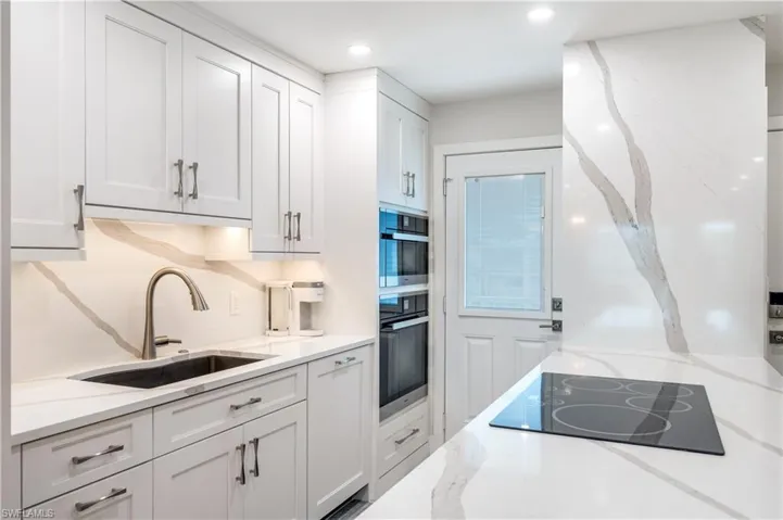 Kitchen featuring white cabinets, light stone counters, black electric cooktop, recessed lighting, and double oven