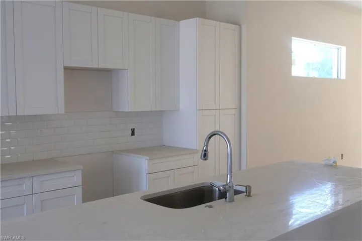 Kitchen with backsplash, white cabinetry, light stone counters, and sink