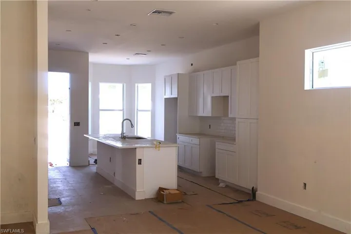 Kitchen with decorative backsplash, a kitchen island with sink, sink, and white cabinets