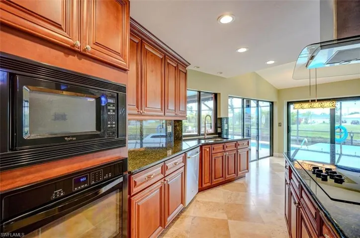 Kitchen with sink, backsplash, dark stone countertops, lofted ceiling, and black appliances