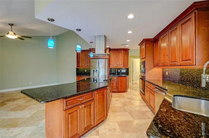 Kitchen featuring a center island, stainless steel appliances, ceiling fan, and dark stone countertops