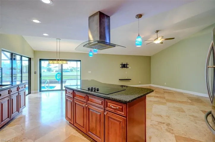 Kitchen featuring island exhaust hood, black electric stovetop, vaulted ceiling, ceiling fan, and decorative light fixtures