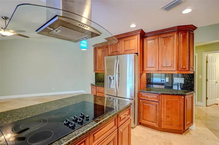 Kitchen featuring decorative backsplash, ceiling fan, dark stone countertops, black electric cooktop, and stainless steel fridge with ice dispenser