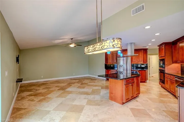 Kitchen with island exhaust hood, black appliances, decorative light fixtures, dark stone countertops, and a center island