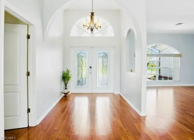 Foyer entrance with french doors, wood finished floors, a chandelier, plenty of natural light, and a towering ceiling