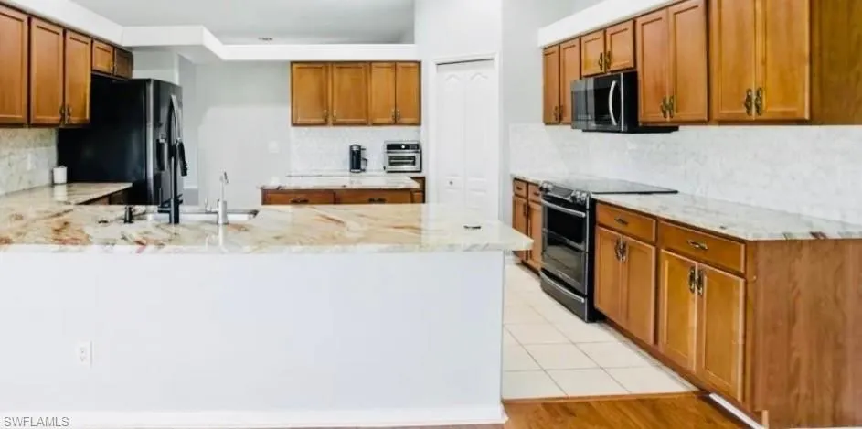 Kitchen with brown cabinets, a peninsula, stainless steel appliances, light stone countertops, and tasteful backsplash