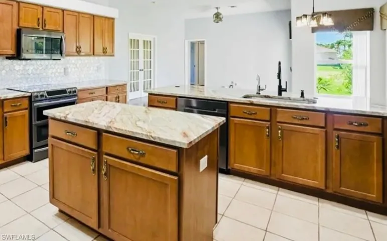 Kitchen with a kitchen island, appliances with stainless steel finishes, light stone counters, and light tile patterned flooring