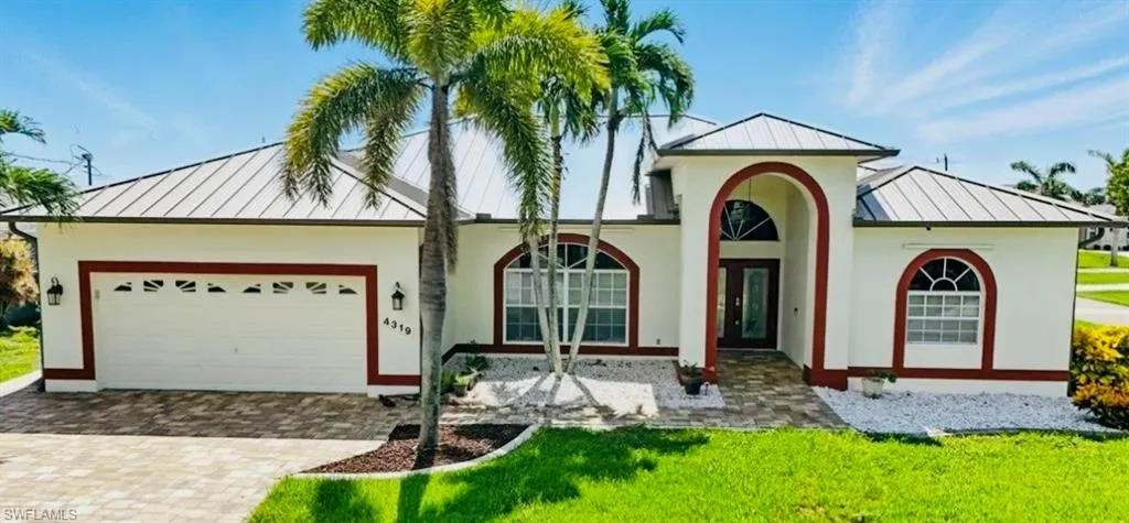 View of front facade with a standing seam roof, a metal roof, a garage, decorative driveway, and a front lawn