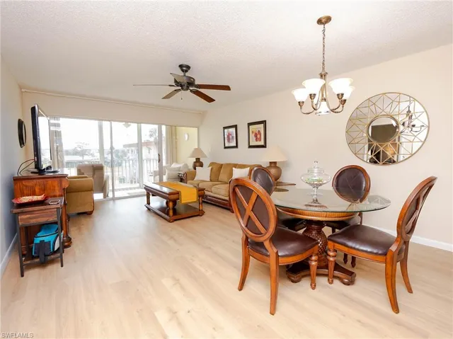 Dining space with ceiling fan with notable chandelier, a textured ceiling, and light hardwood / wood-style flooring