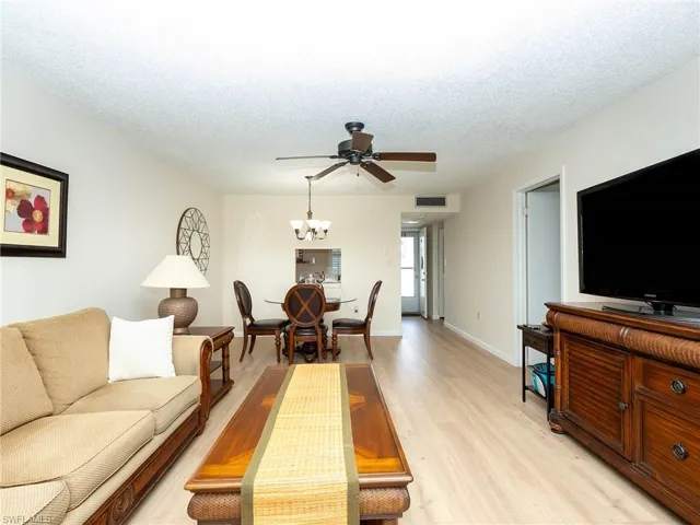 Living room featuring a textured ceiling, ceiling fan with notable chandelier, and light hardwood / wood-style flooring