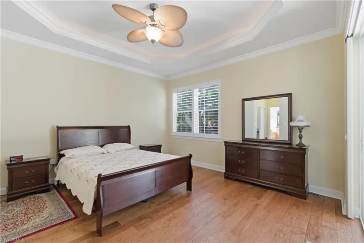 Bedroom with a tray ceiling, ornamental molding, light wood-type flooring, and a ceiling fan