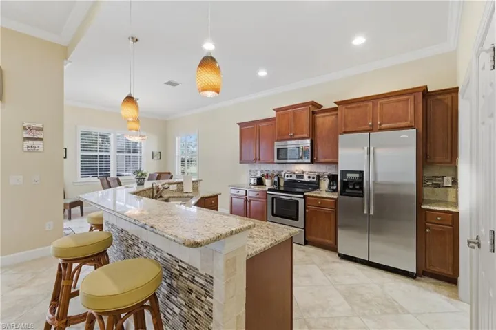 Kitchen featuring appliances with stainless steel finishes, ornamental molding, a breakfast bar area, pendant lighting, and tasteful backsplash