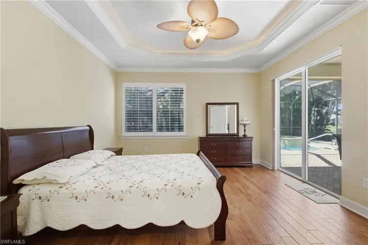Bedroom featuring wood-type flooring, crown molding, access to exterior, ceiling fan, and a raised ceiling