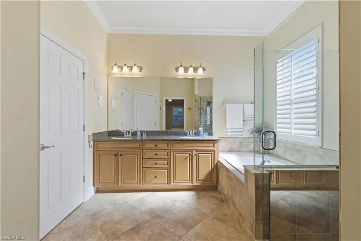 Bathroom with double vanity, a garden tub, ornamental molding, and a stall shower