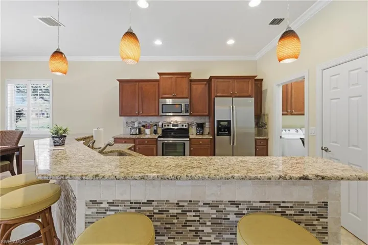 Kitchen featuring a breakfast bar, stainless steel appliances, tasteful backsplash, light stone countertops, and washer / dryer