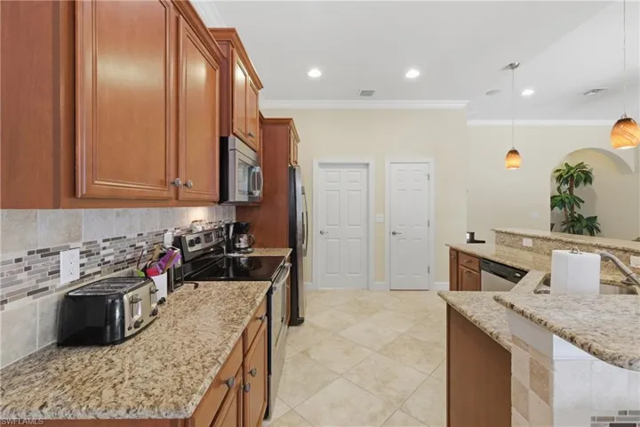 Kitchen featuring stainless steel appliances, brown cabinetry, hanging light fixtures, a kitchen island with sink, and crown molding