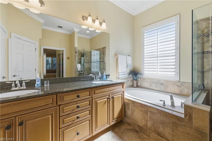 Bathroom with crown molding, a bath, a stall shower, and double vanity
