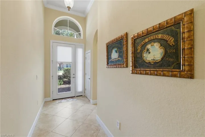 Entryway featuring light tile patterned floors, ornamental molding, a textured wall, and a towering ceiling
