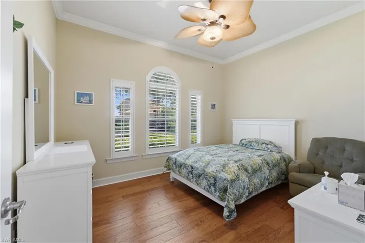 Bedroom with ornamental molding, dark wood-style flooring, and ceiling fan