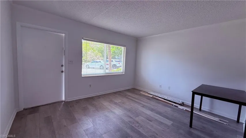 Spacious room featuring wood-finish flooring, white walls, and a large window with blinds