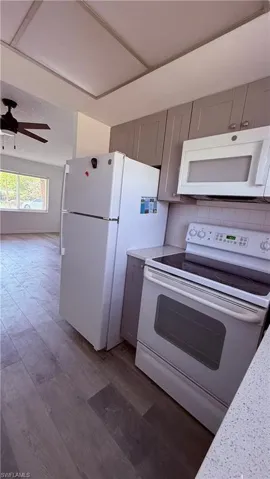 Kitchen featuring white appliances, gray shaker-style cabinetry, a white subway tile backsplash, and light wood-finish flooring