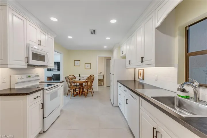Kitchen with light tile patterned floors, white appliances, sink, and white cabinets